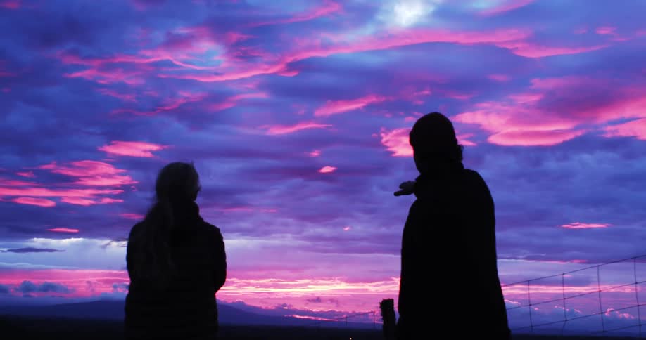 Silhouette of two people looking out at the horizon at sunrise