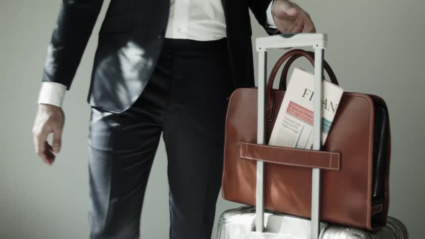 A man places a briefcase on top of a luggage handle