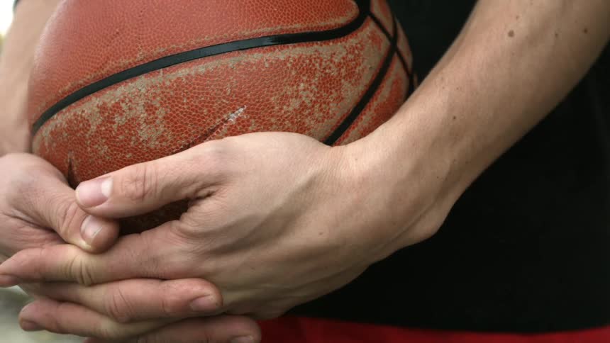 A white man stands outdoors cradling a basketball in his hands