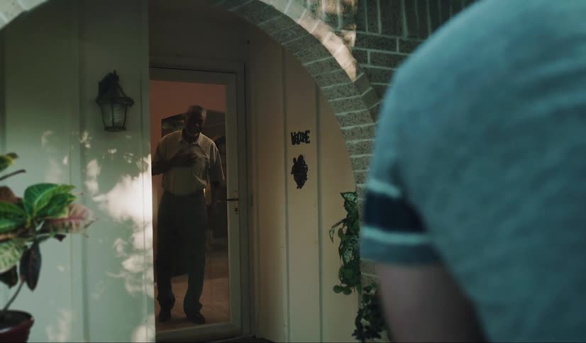 Man and young boy deliver boxed items to a black man waiting in the doorway of a house
