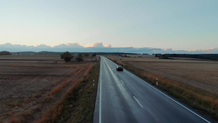Aerial view of a black car driving on a highway on the plains at dusk