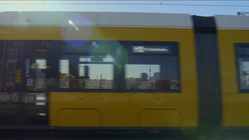 A train goes past some people walking on the sidewalk