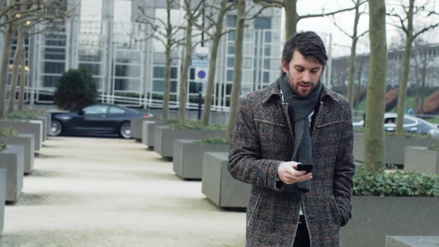 A man walks down a sidewalk while looking at his smart phone