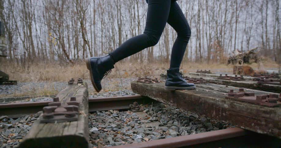 A person walking on train tracks with trees and the sky in the background
