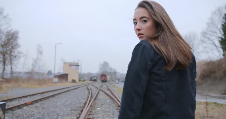 A young white woman walks along railroad tracks