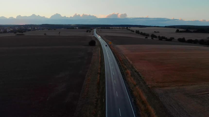 Aerial view of a black car driving on a highway stretching across plains