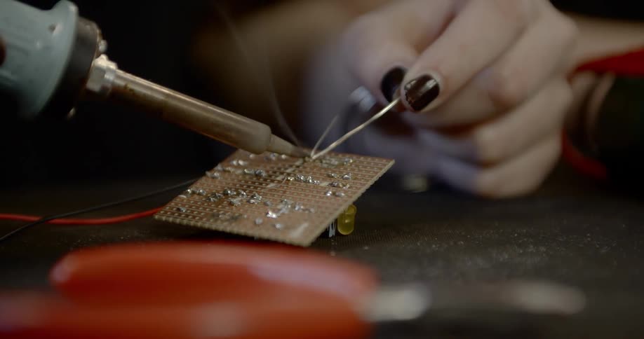 Person with dark fingernail polish solders wire onto small circuit board