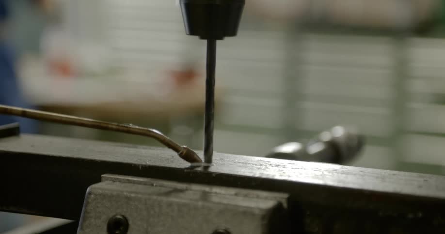 Man oils metal surface to drill it with a power took in a workshop