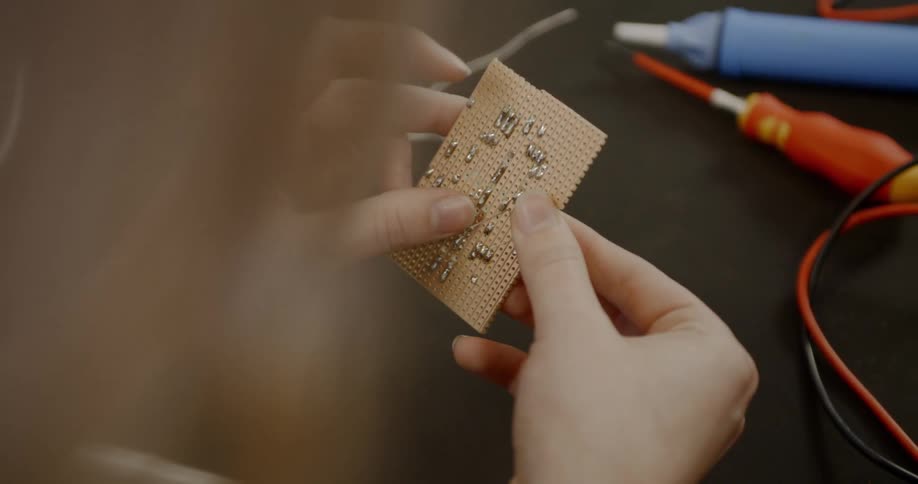 Woman manipulates a board electronic components in a working bench