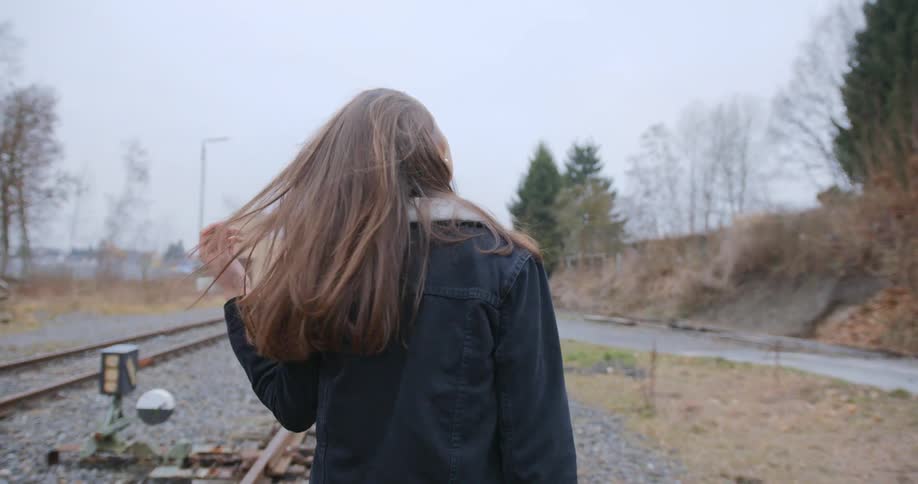A young woman runs her hand through her hair as she walks down train tracks