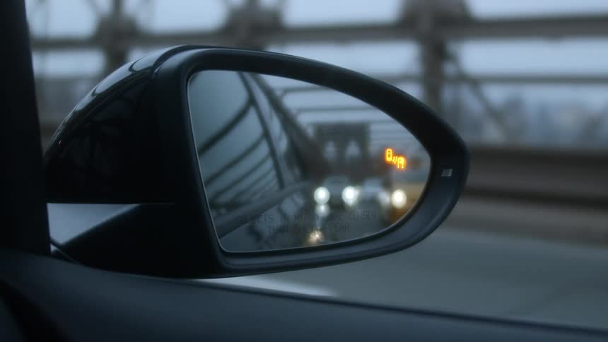 A vehicle with a mirror with the reflection of a bridge and vehicles
