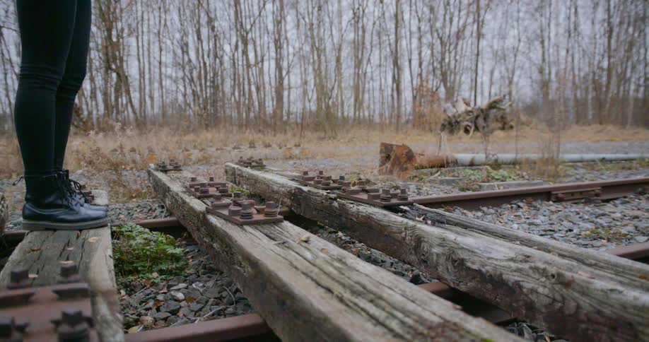 A person stands on the rotted train track by the forest