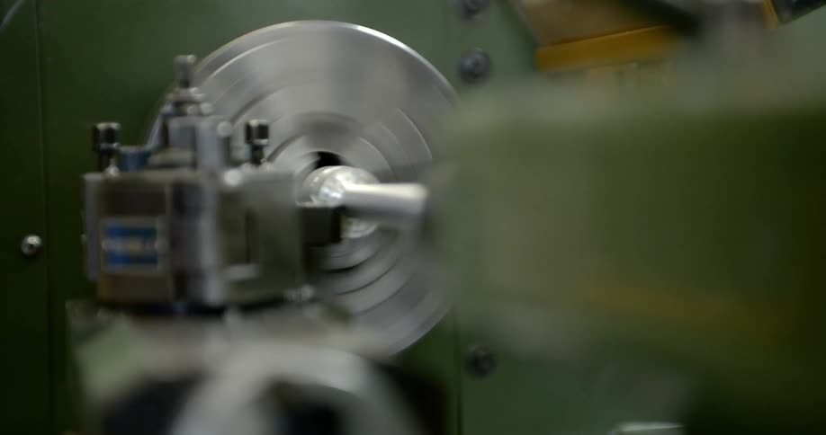 Metal shavings fall as a metal lathe shapes a piece of metal