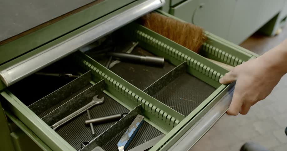 A person opens a metal drawer to withdraw several tools