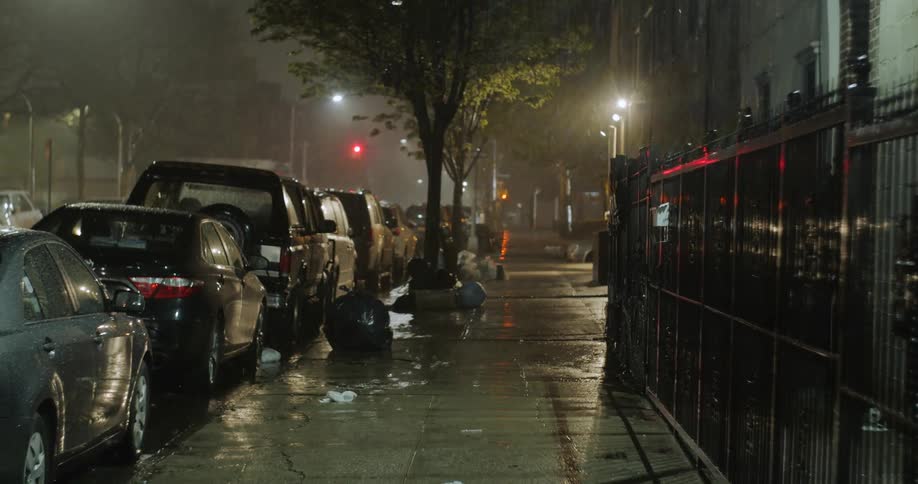 Vehicles parked at the side of a city road at night as the rain falls