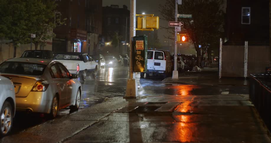 Vehicles drive down a city street thats still wet from rain