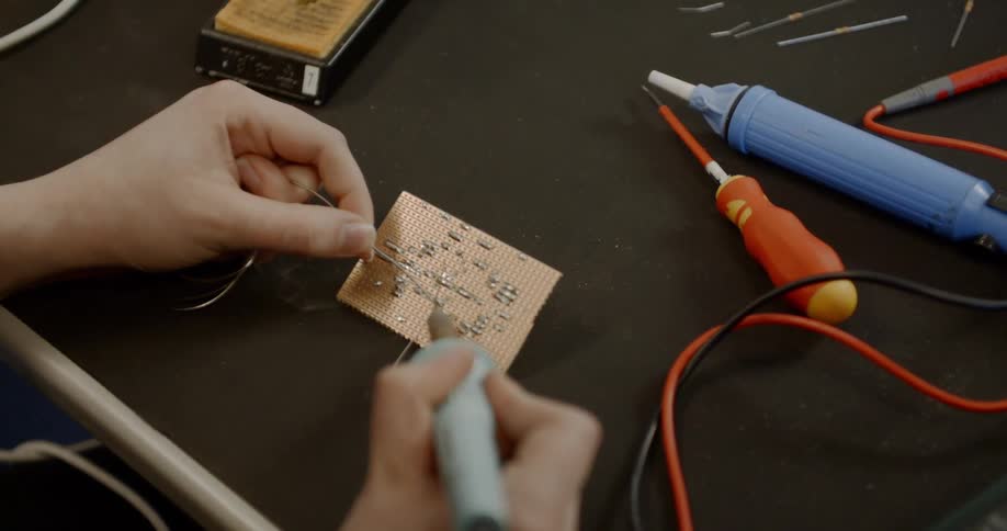 A white man uses a soldering gun on a small circuit board