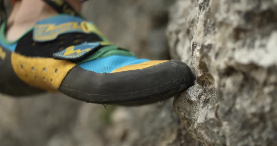Foot in climbing shoe gains foothold on rock face