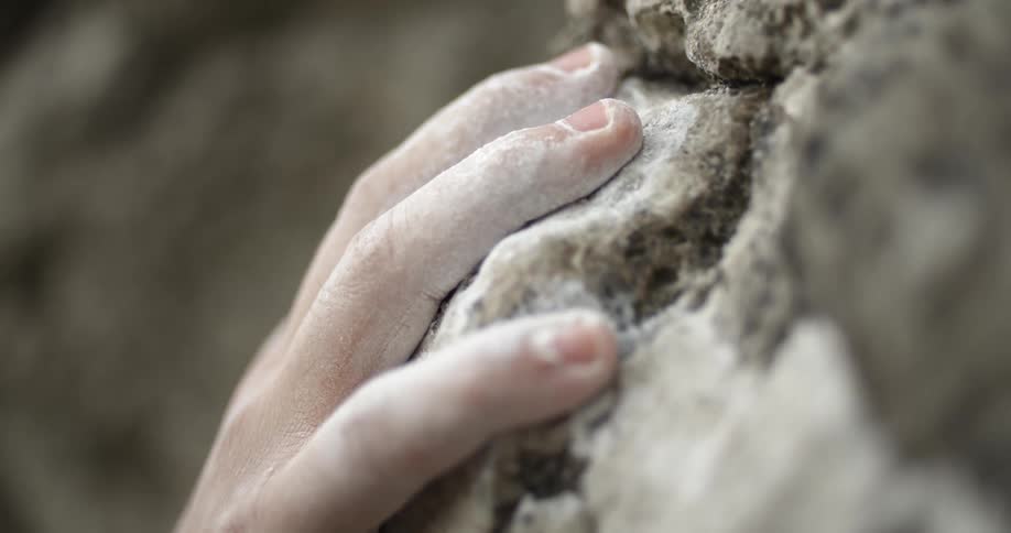 A person grabs onto a rock as they climb a rock formation