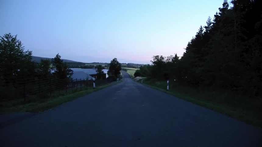 A country road with trees silhouetted against the sky at dusk