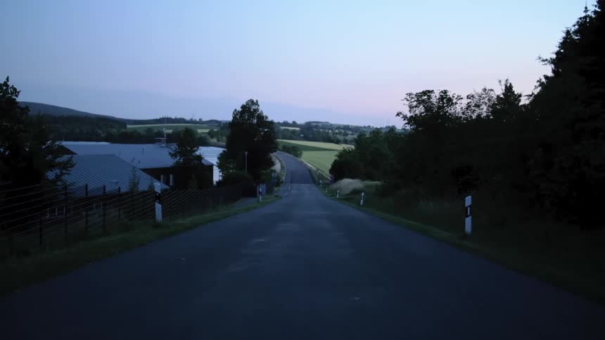 A country road with trees silhouetted against the sky at dusk