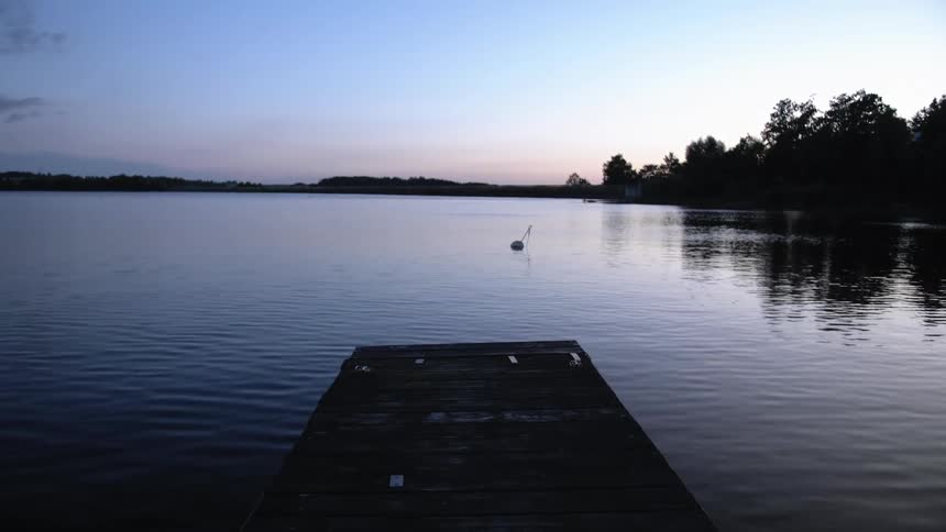 Small boat floats in the lake near the trees at dusk