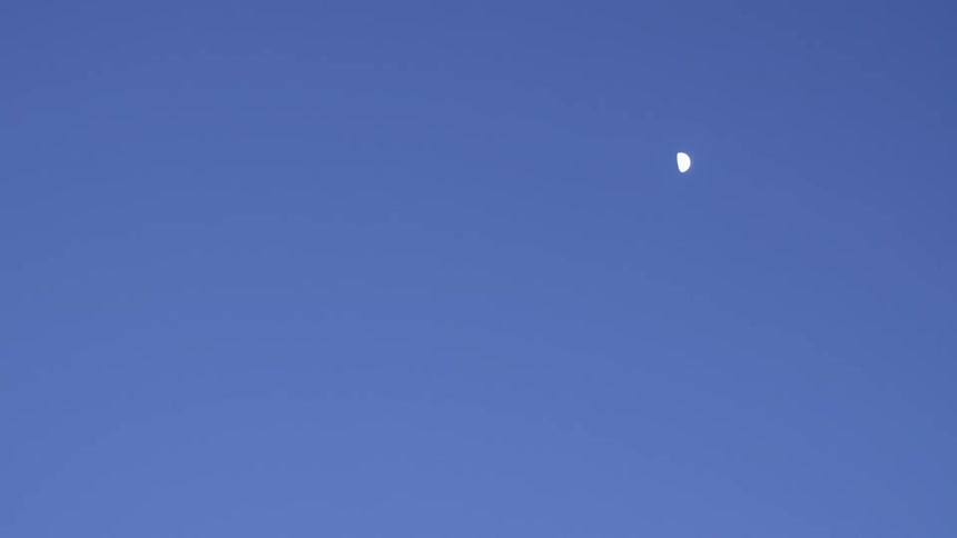 Half moon occupies clear blue sky