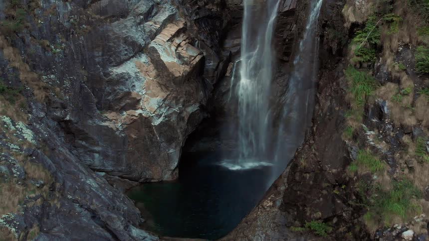 Water falls over a cliff in a canyon into a blue river