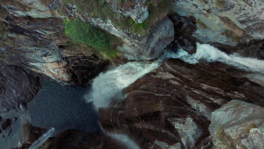 Aerial view of a water fall streaming down the rocks of a rock cliff in to a river