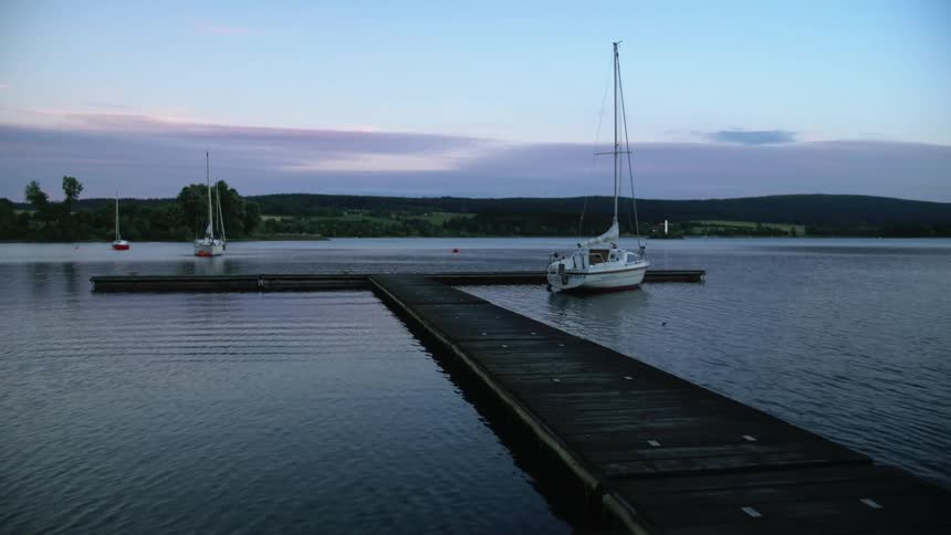 A sailboat sits near a dock while two other boats float out in the lake