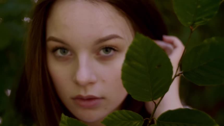 Young woman looks into camera from behind leaves