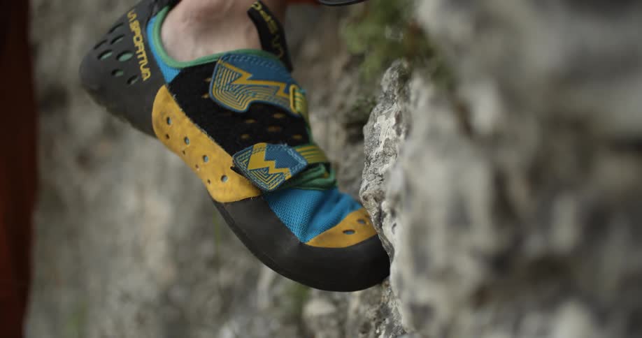A person climbs a mountain side while wearing climbing gear