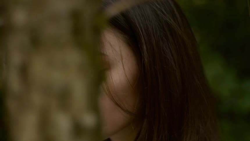 Teenage girl with straight and black hair glances at the camera in the forest