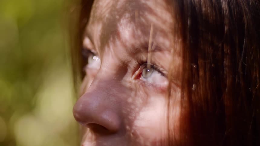 A woman staring and looking up with the sun shining on her face with trees in the background