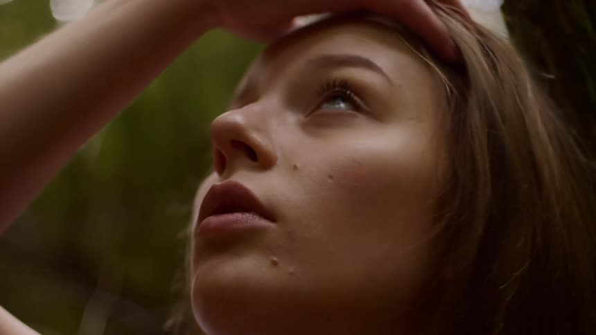 A woman with her head tilted back and looking up runs her fingers through her hair