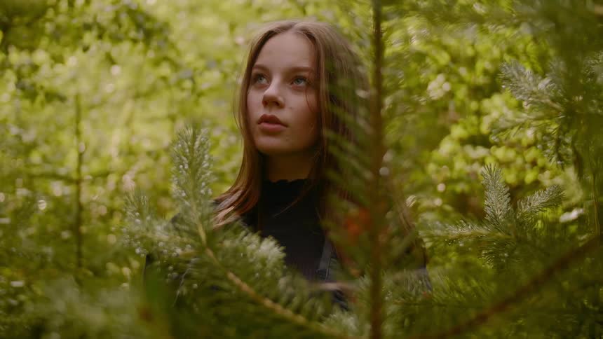 Young woman with long hair poses between the pines in a forest