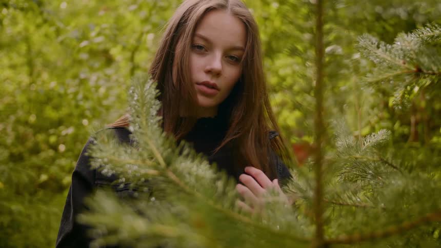 A woman in a forest staring surrounded by trees