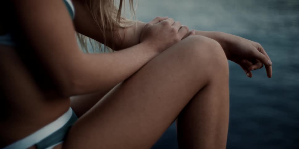 A white woman in a bikini sits near a body of water