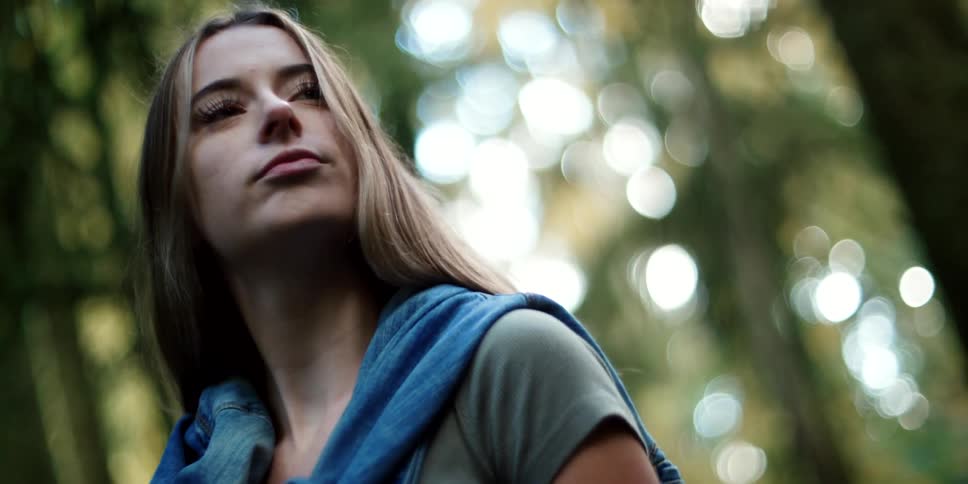 Woman with brown hair and freckles stands out against the blurry background and walks in the forest