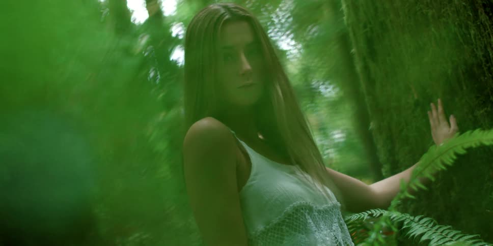 A woman standing in the woods with her hand on a tree trunk surrounded by trees