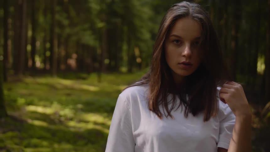 Young woman on a white shirt walks in a forest looking at the camera
