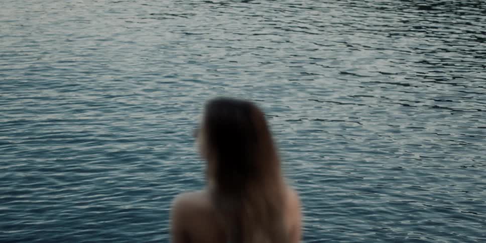 A white woman stands in front of a rippling body of water