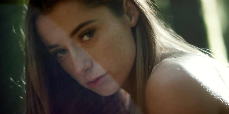 A young woman poses in front of trees as sunlight washes over her