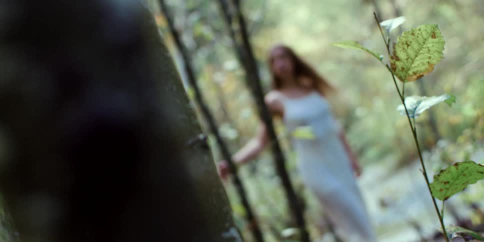 Woman with brown hair and a white dress walks in the woods