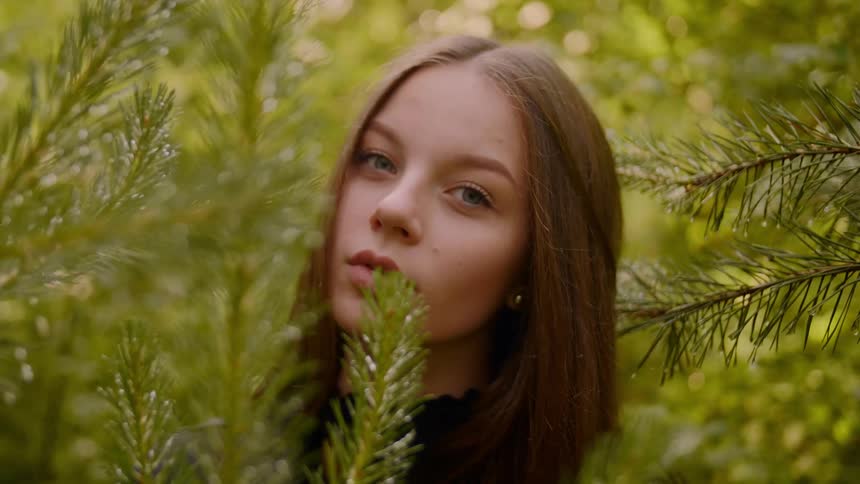 A woman stands behind the branches in the forest