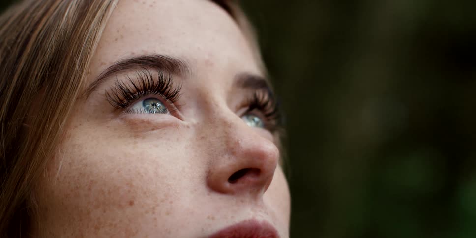 Woman with brown hair and freckles looks up at the sky