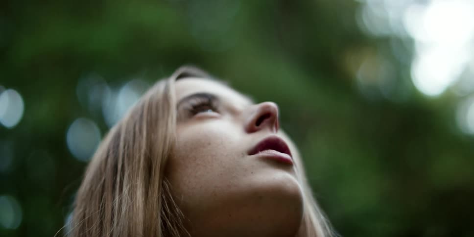 Woman in a white dress stands in a forest looking up