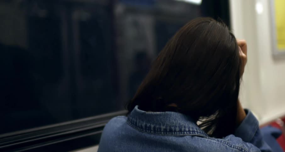 Young woman riding subway rests head against hand