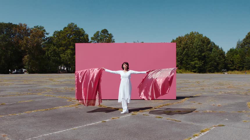 A woman dances with two flags in an empty parking lot
