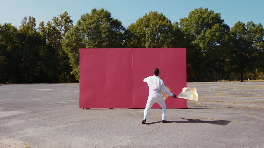 A young black man dances and waves flags in front of a red billboard